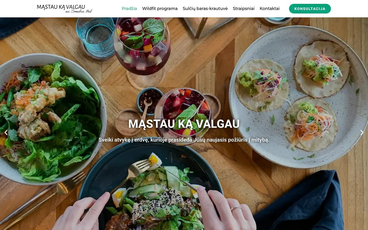 Mąstau ką valgau homepage with an overhead photo of salads, tacos and beetroot drinks on a wooden table and the site name as the heading