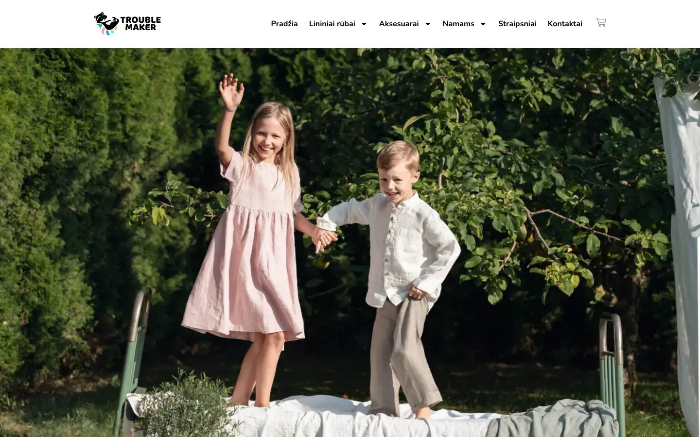 Trouble Maker homepage with two children in linen clothes playing on a bed set up in a green garden, under a menu of linen clothing, accessories and home categories
